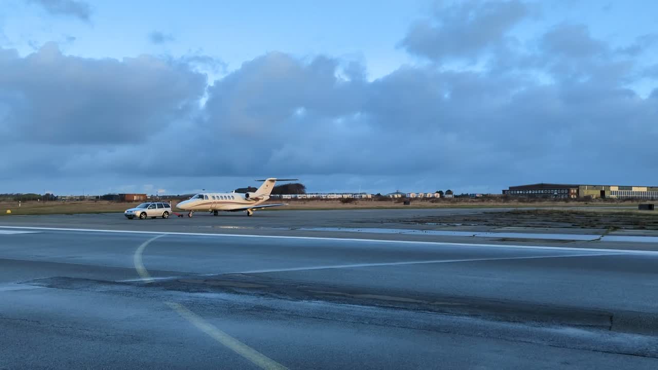 A light jet crossing a wet runway under a dusk sky
